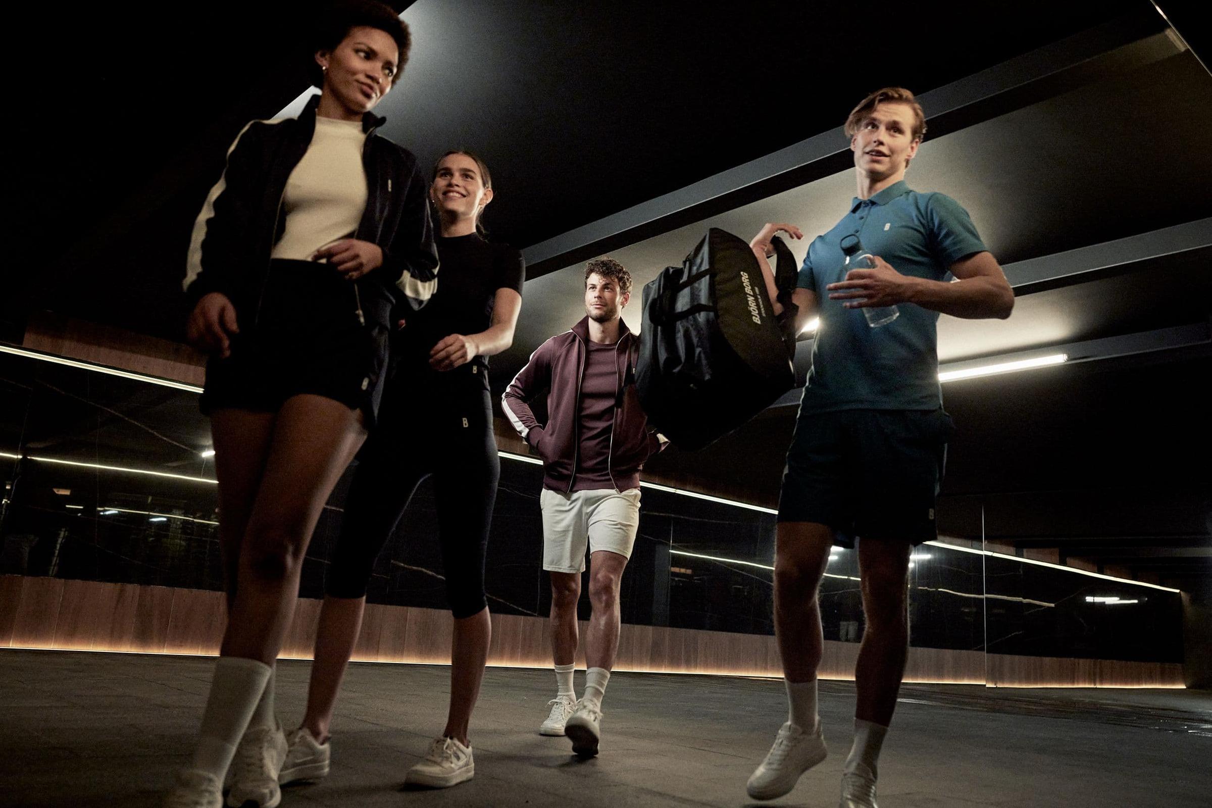 Fire unge voksne kledd i sportsutstyr som går selvbevisst i en moderne bymiljø.