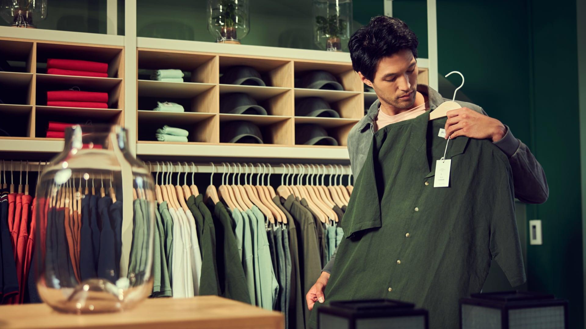 Una persona examina una camisa verde con una etiqueta de precio en una tienda de ropa.