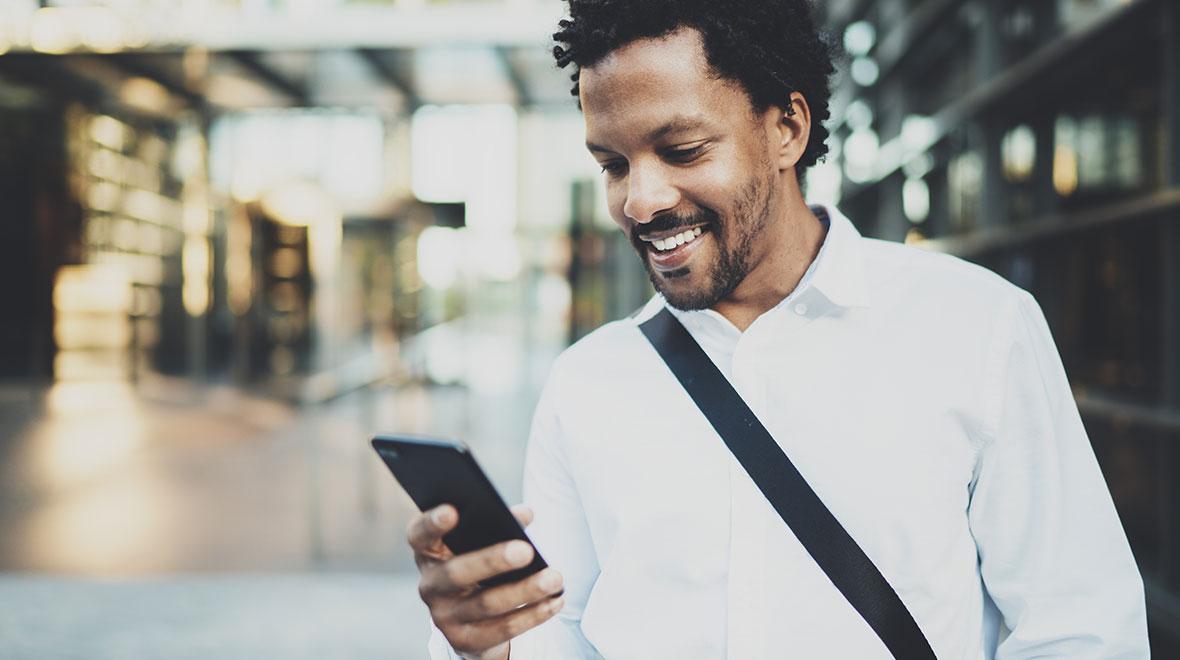 Homem sorrindo usando smartphone em um corredor de prédio moderno e iluminado.