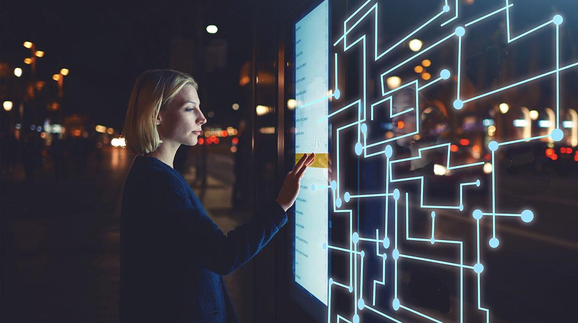 Mujer interactuando con una interfaz digital iluminada en una calle de la ciudad por la noche.