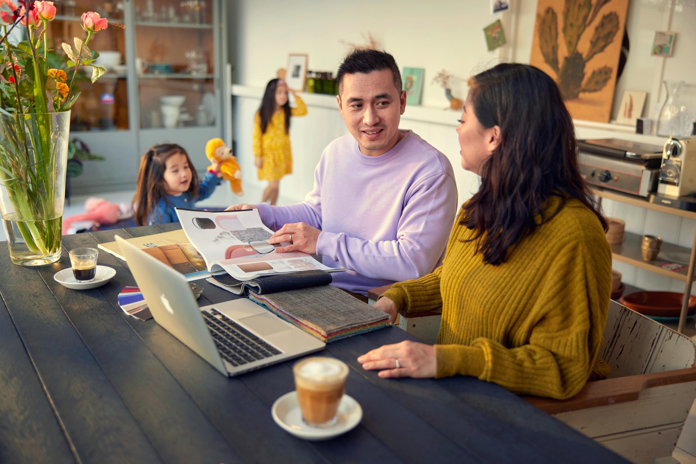 Couple with kids sitting at a table in front of a laptop choosing a fabric for their home furnishing.