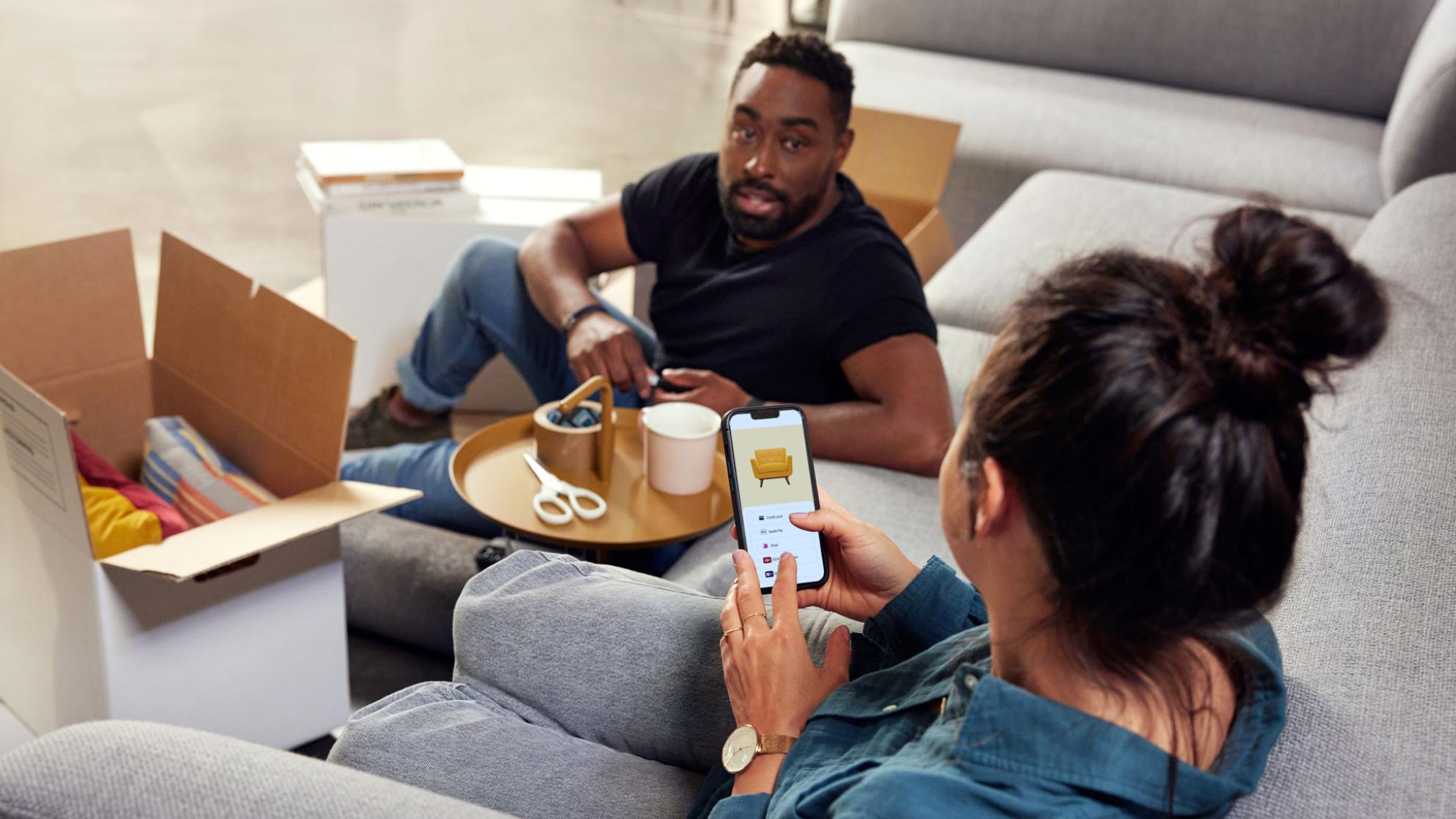 Uomo seduto dietro una donna che fa shopping online sul suo smartphone