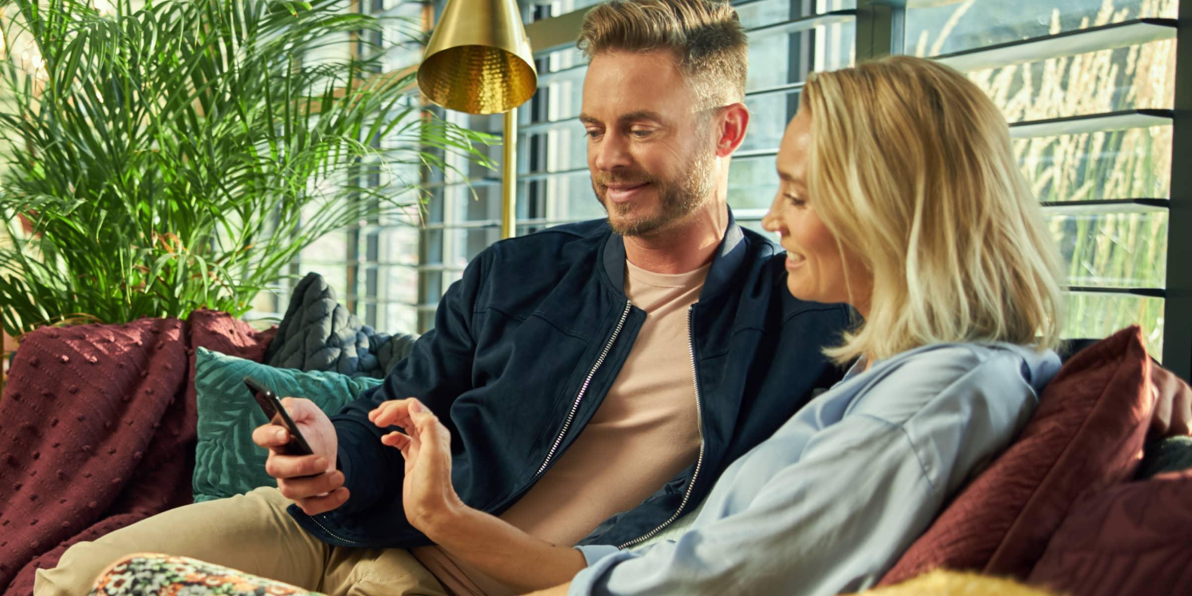 Two people sitting comfortably on a couch with one holding a smartphone.