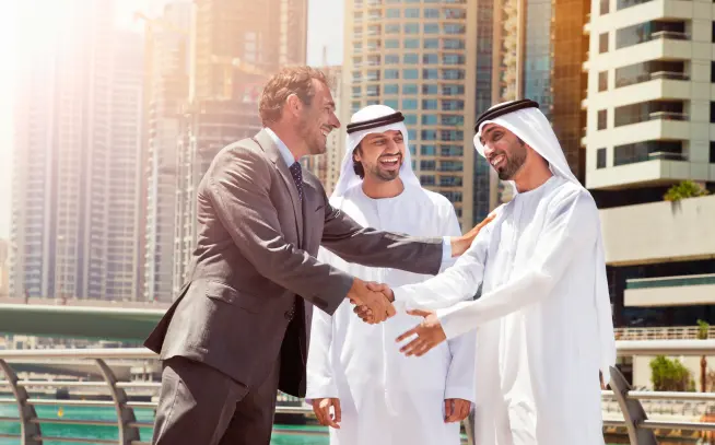 3 arabic people having a conversation ad shaking hands. Surrounded by tall dubai buildings