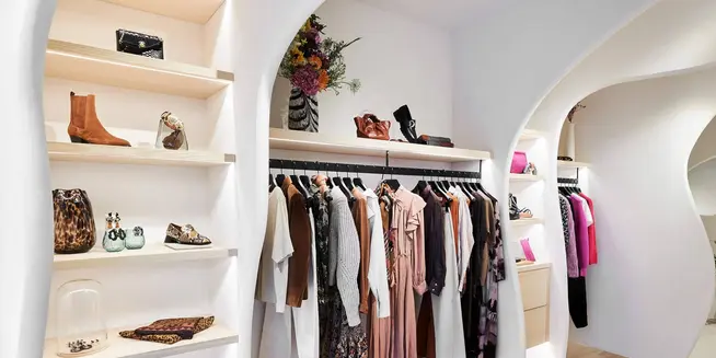 Intérieur de boutique élégant présentant des vêtements, des chaussures et des accessoires sur des étagères et des cintres.