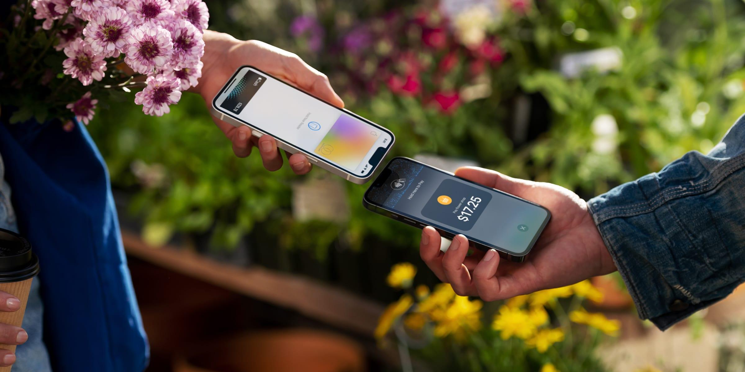 Two hands holding smartphones, one performing a contactless payment to the other amidst plants.