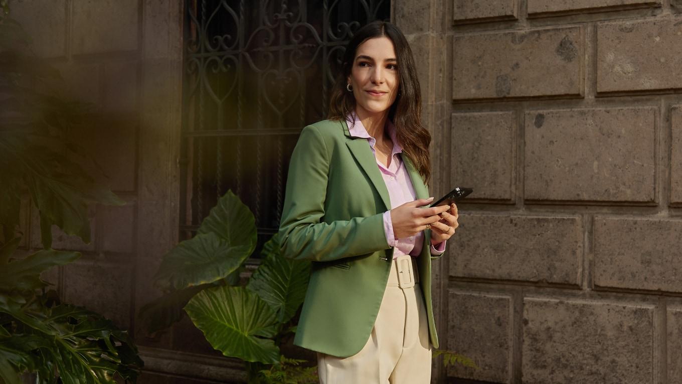 Pewna kobieta w zielonej marynarce trzymająca smartfona.