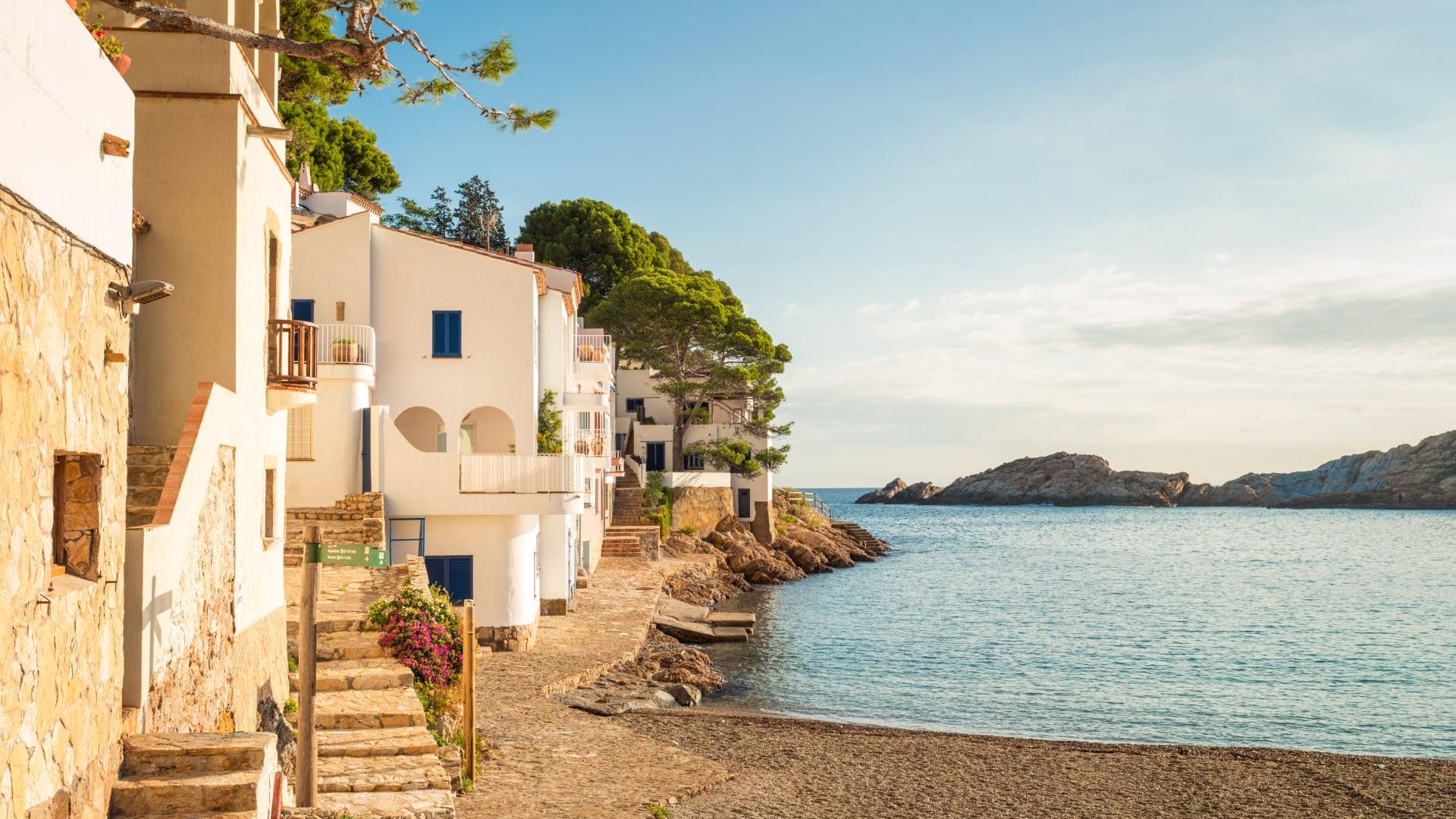 Seaside view with sandy beach and coastal houses under a clear sky at sunset in Spain.