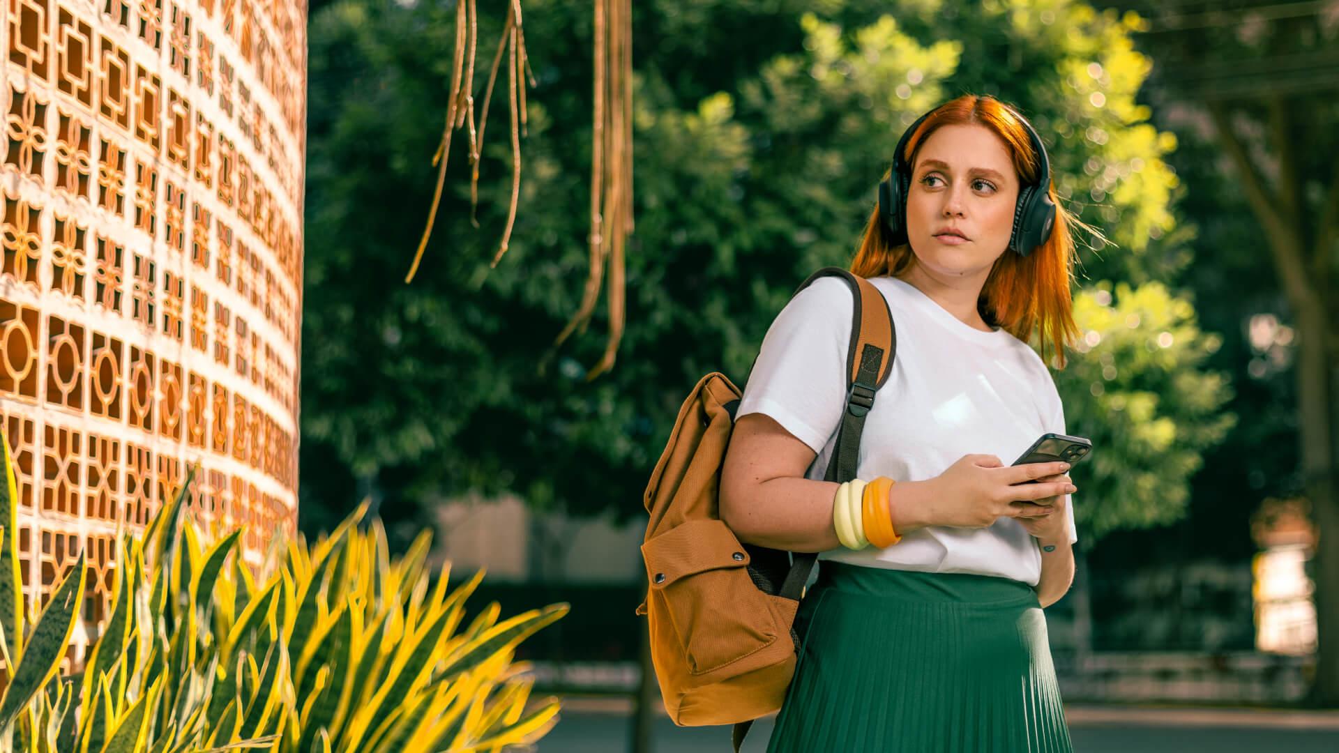 Mulher com mochila e fones de ouvido usando um smartphone em uma rua da cidade ensolarada