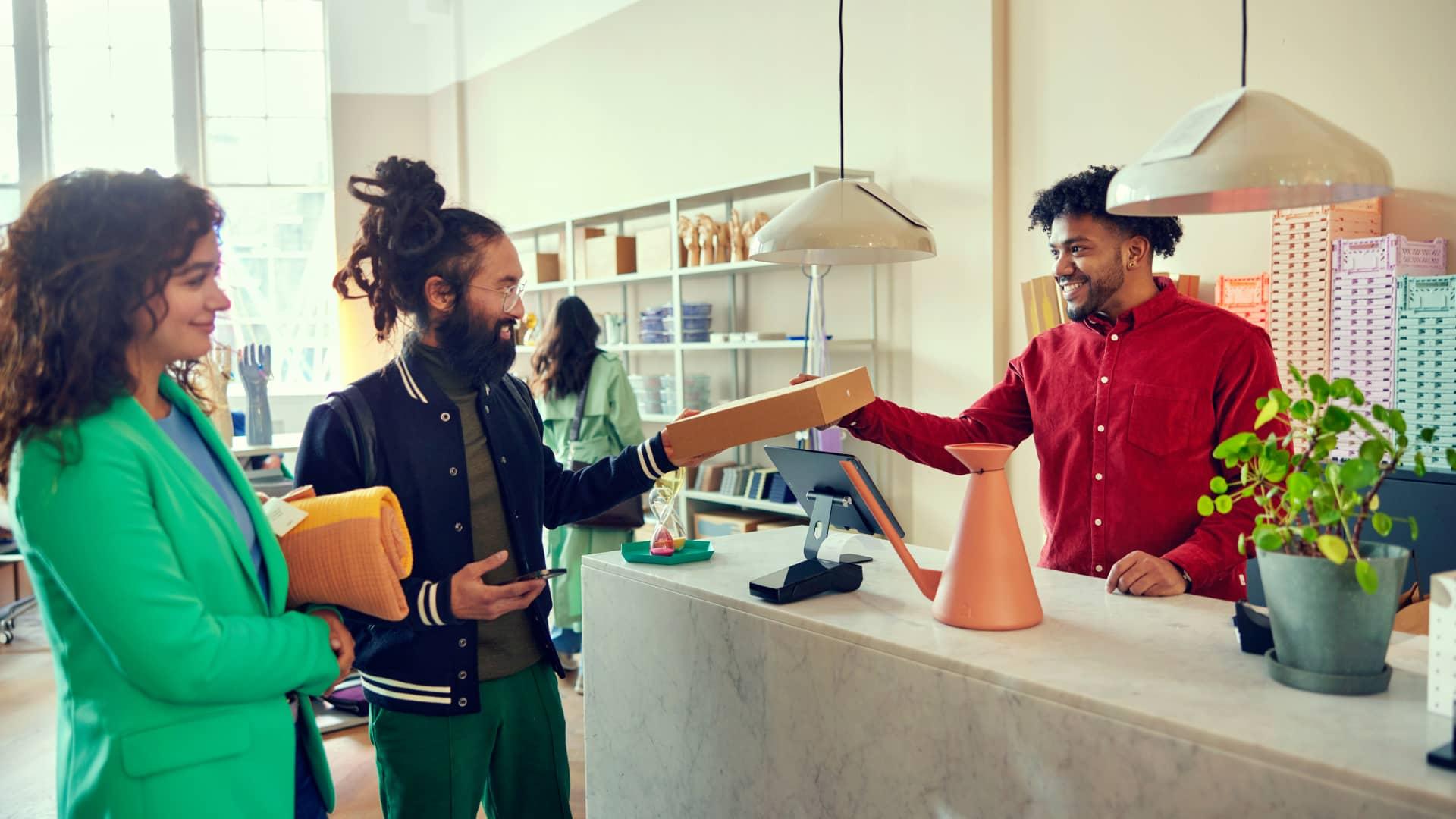 Smiling store assistant handing over a package to a happy customer at a homeware boutique checkout.