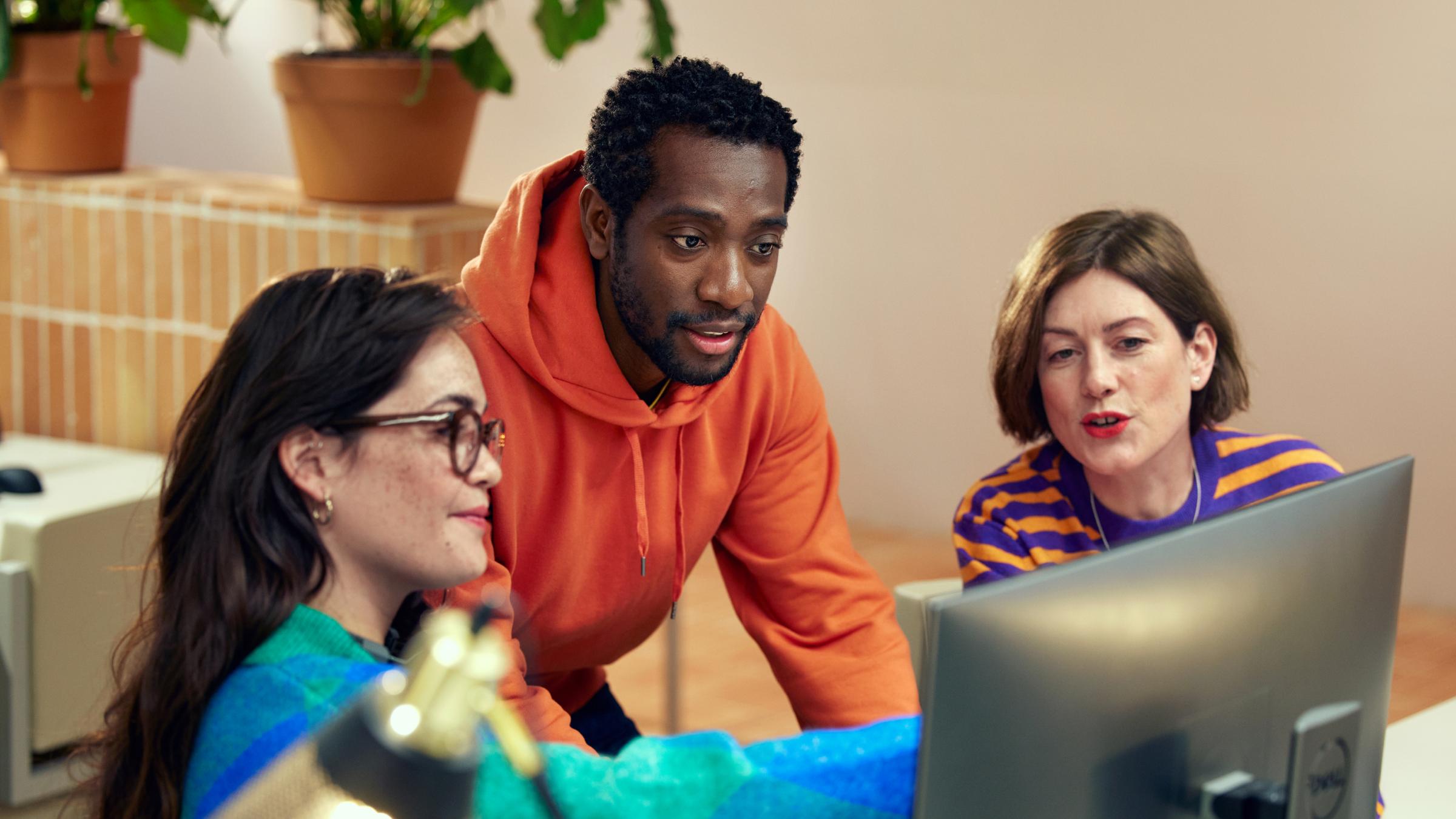 Three colleagues collaborating on a project around a computer screen.