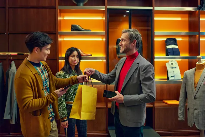 A couple in a luxury fashion store receiving a paper bag with their purchase after payment.