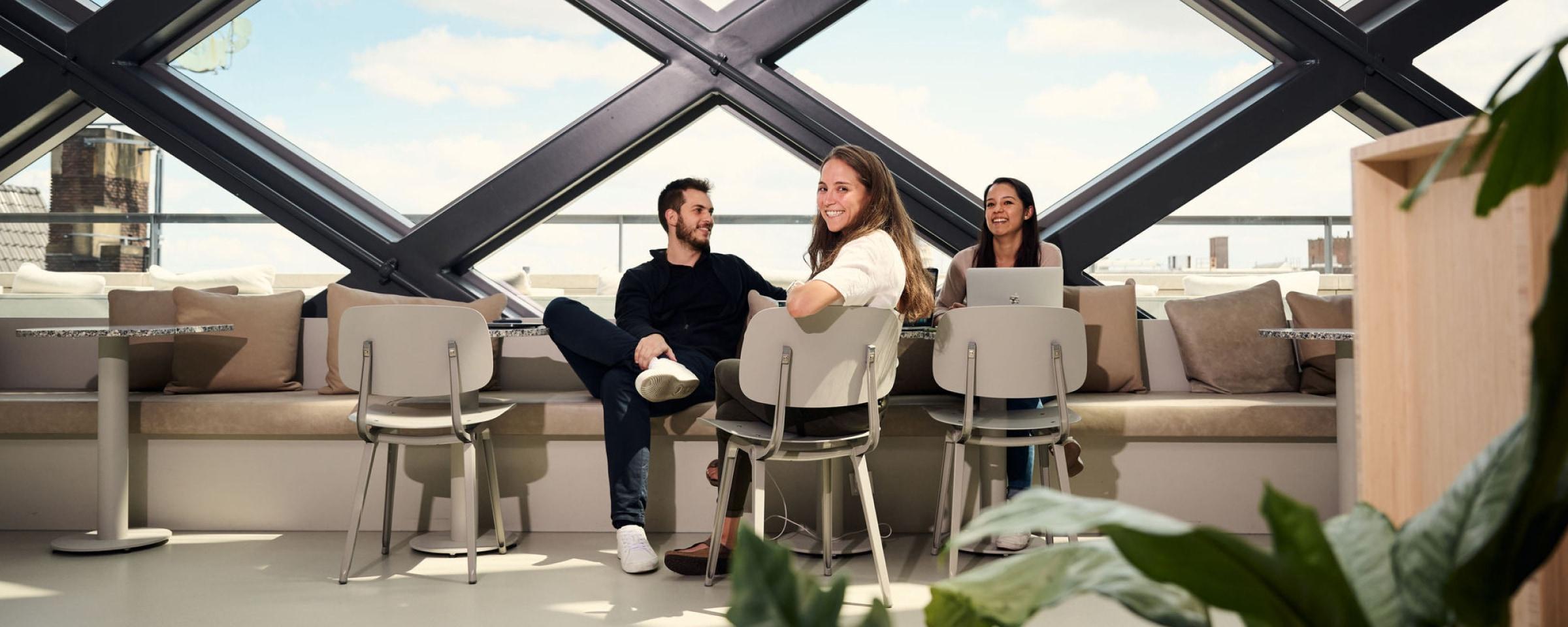 Tre kolleger som samhandler uformelt på et moderne kontor med bærbare datamaskiner.