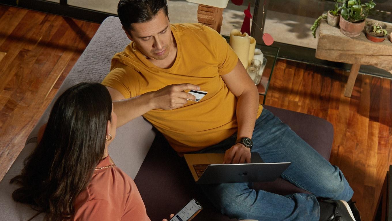 Duas pessoas sentadas discutindo em laptops com um cartão de crédito na mão.