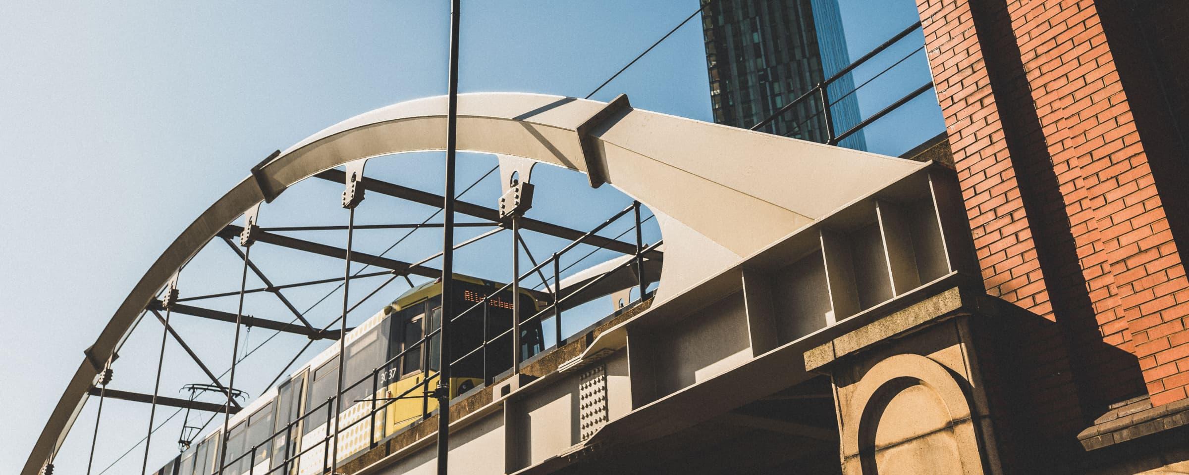 Modern tram arriving at an elevated station with urban architecture in the background.