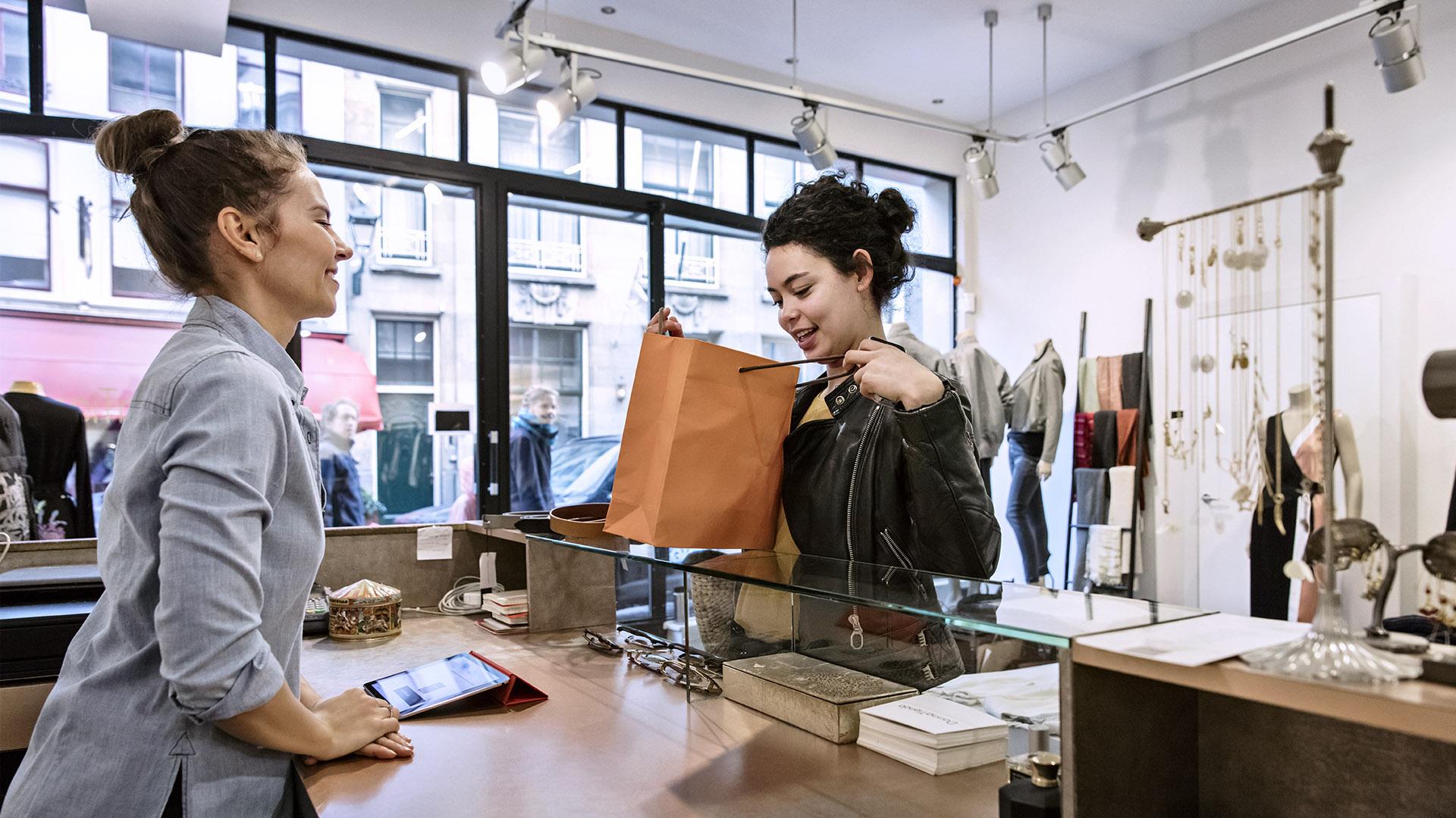 Nöjd kund som tar emot en shoppingbag över disken med Adyen-betaltillstånd