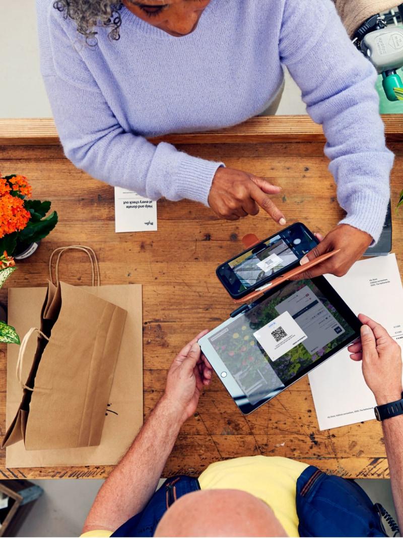 Duas pessoas usando a plataforma de pagamento da Adyen em dispositivos móveis em um balcão de madeira.