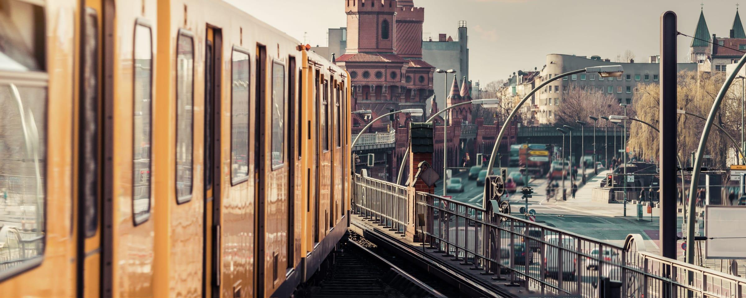En orange tog, der kører på en ophøjet bane i en bymiljø.