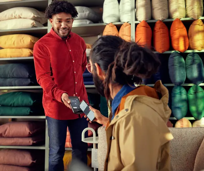 Customer making a contactless payment using a handheld Adyen payment device in a store with decorative pillows.