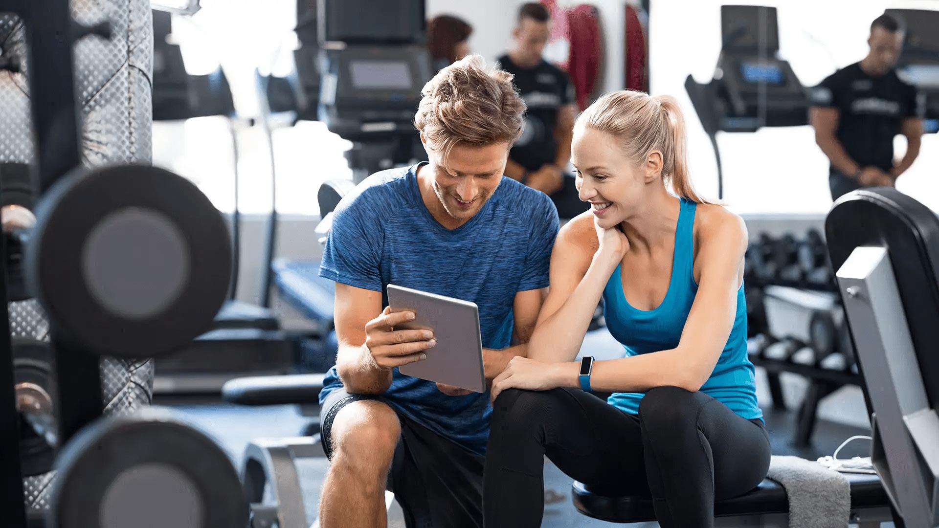 Two people looking at a tablet in a gym setting.