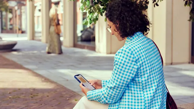 Person sitting on bench using a mobile payment app outdoors.