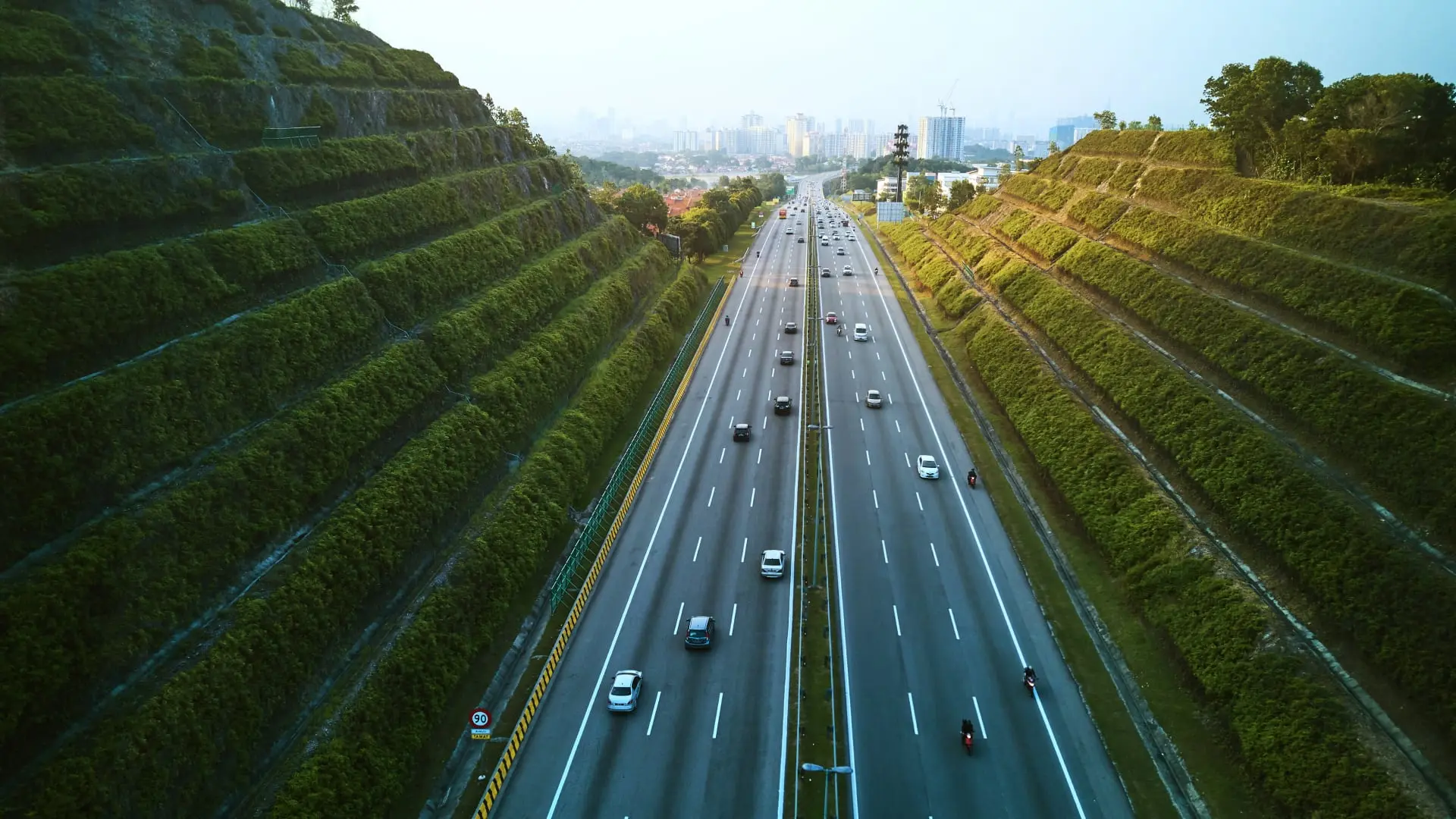 Aerial view of a multi-lane highway with traffic and green terraced slopes on either side in Malaysia.