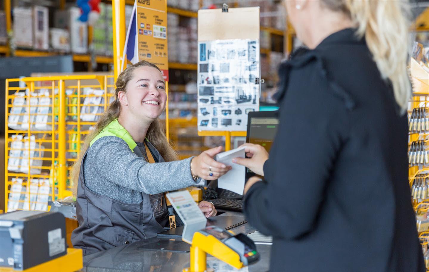Employé souriant remettant un reçu à un client à un comptoir de caisse avec un terminal Adyen.