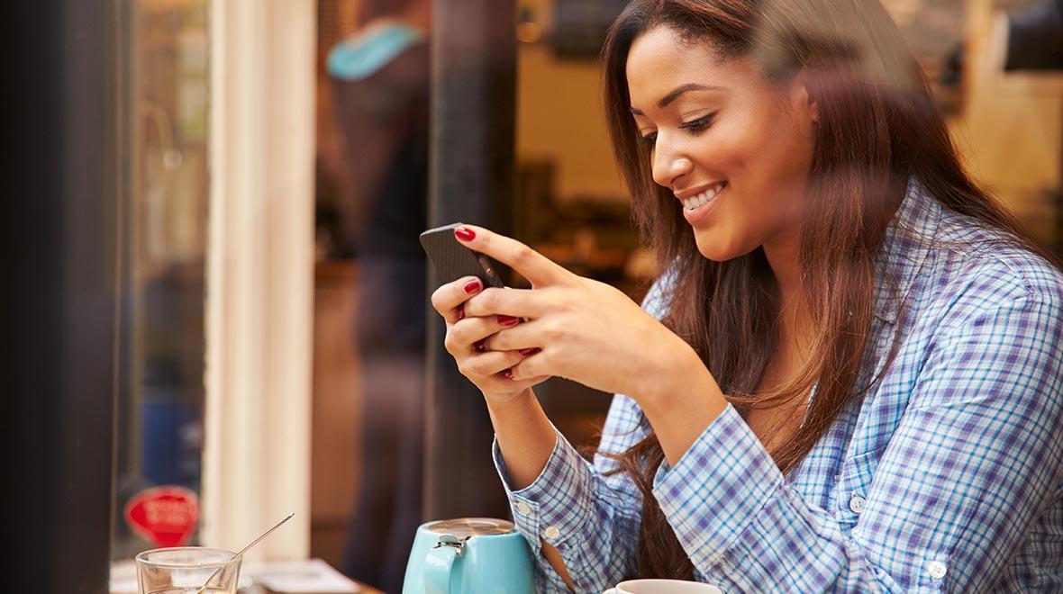 Mulher sorrindo usando um smartphone em uma mesa de café