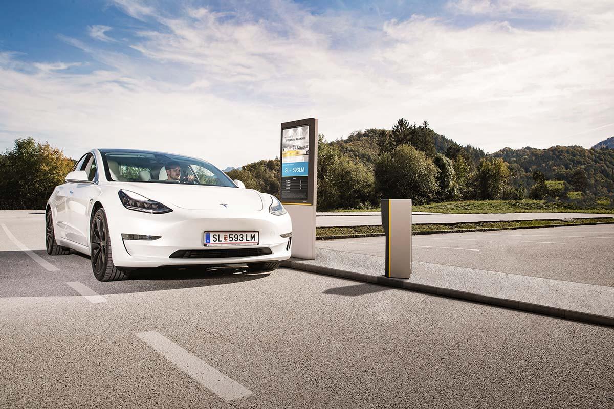 White electric car charging at a roadside station with digital display.