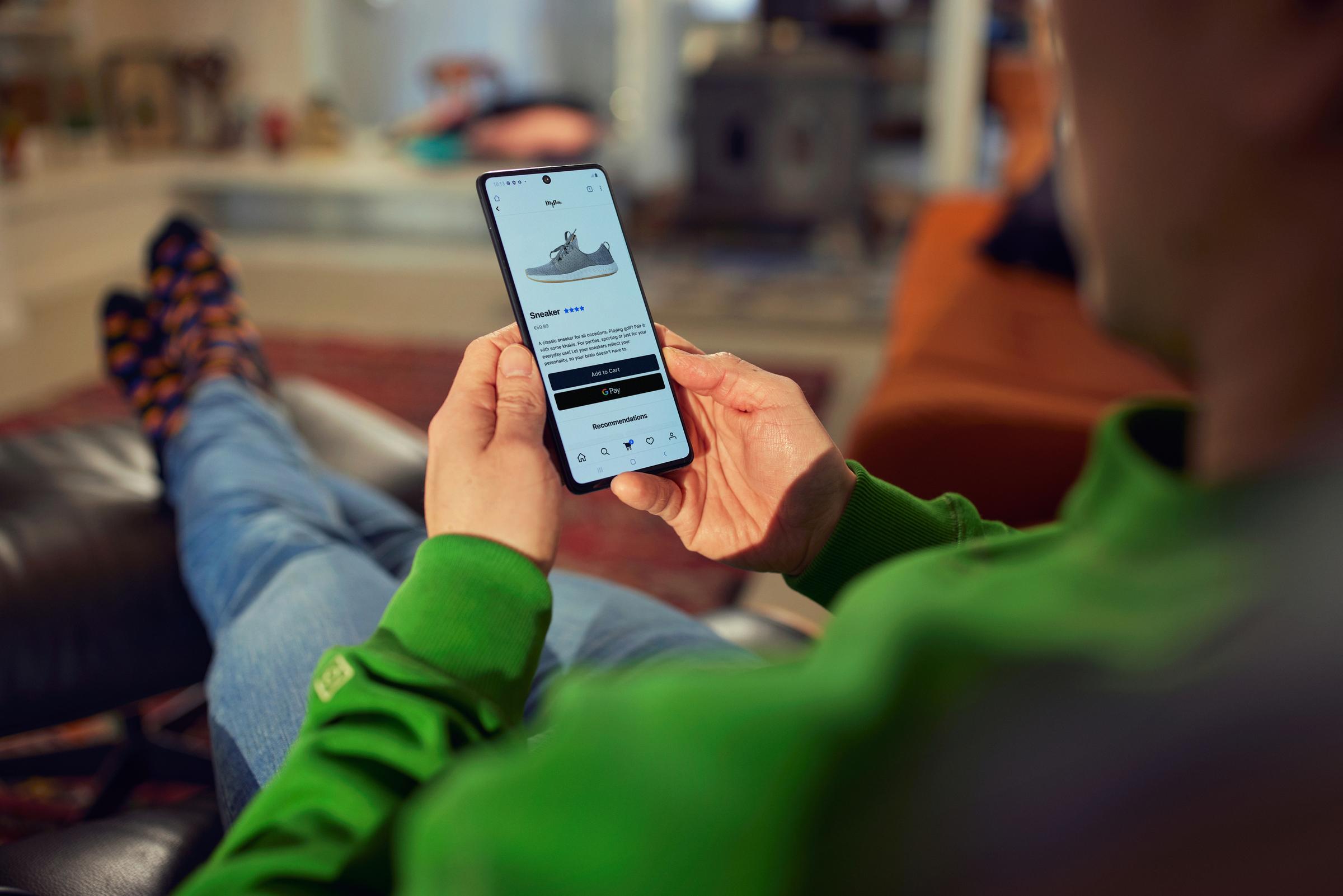 Osoba uśmiechająca się i patrząca na telefon z butem na ekranie kasy w pierwszym planie.