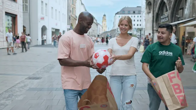 Dva muži a žena si užívají hravý okamžik s fotbalovým míčem na městské ulici.