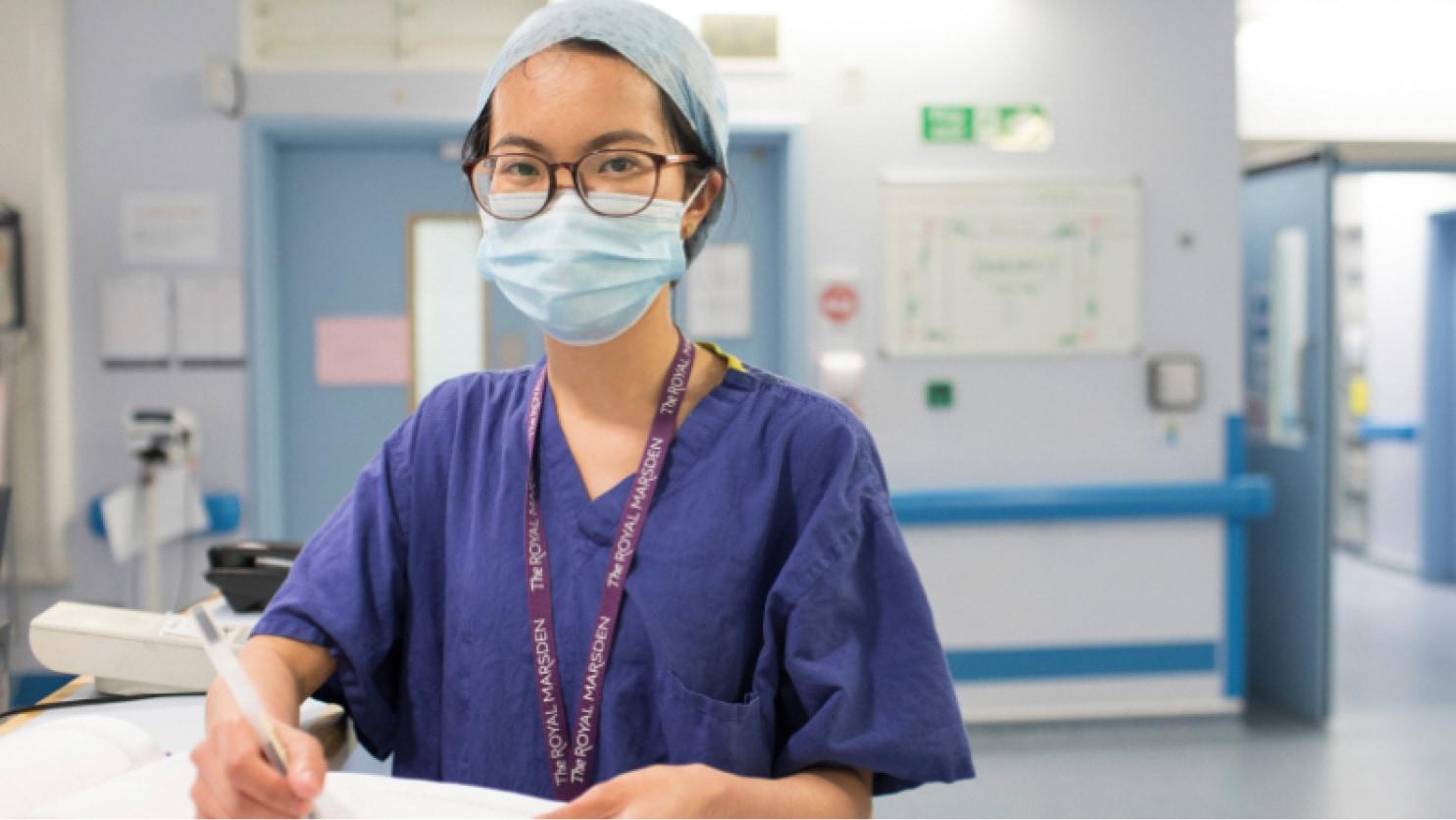 Kvindelig sundhedsfaglig medarbejder i kit og maske gennemgår dokumenter på hospitalets gang.