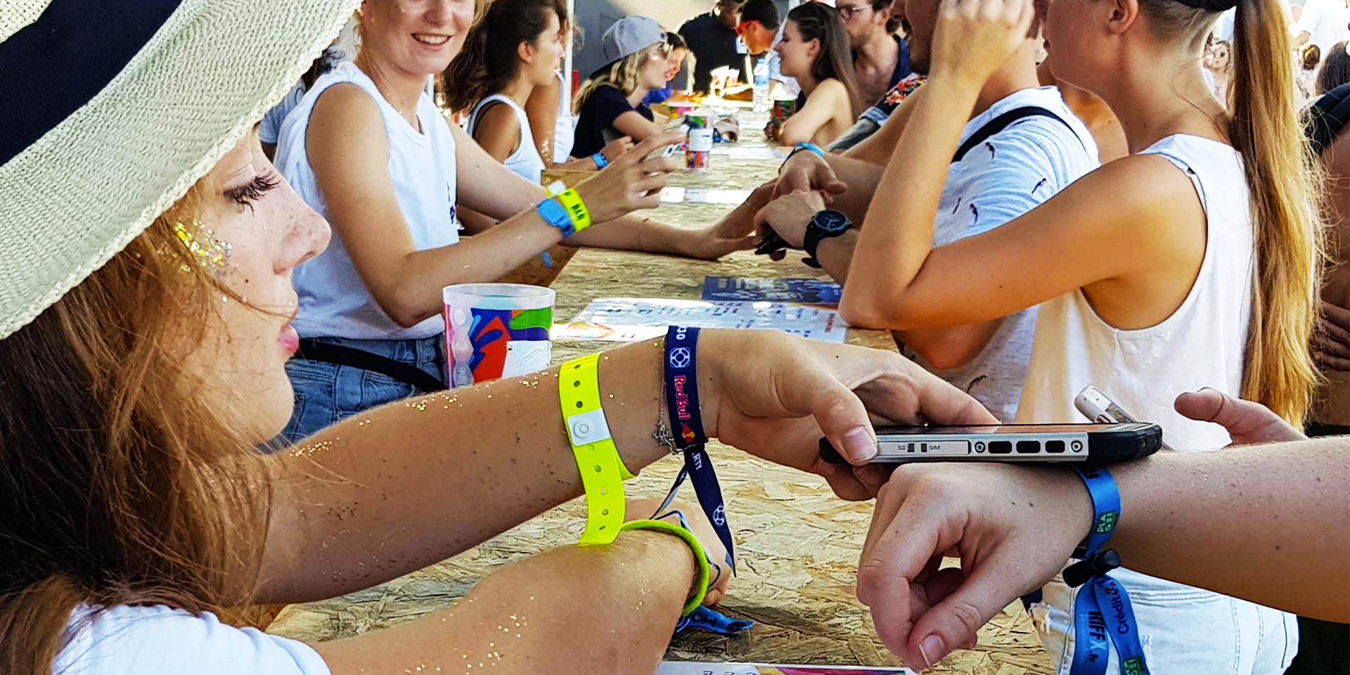 Personne utilisant un dispositif de paiement mobile pour traiter une transaction de bracelet à un événement en plein air.
