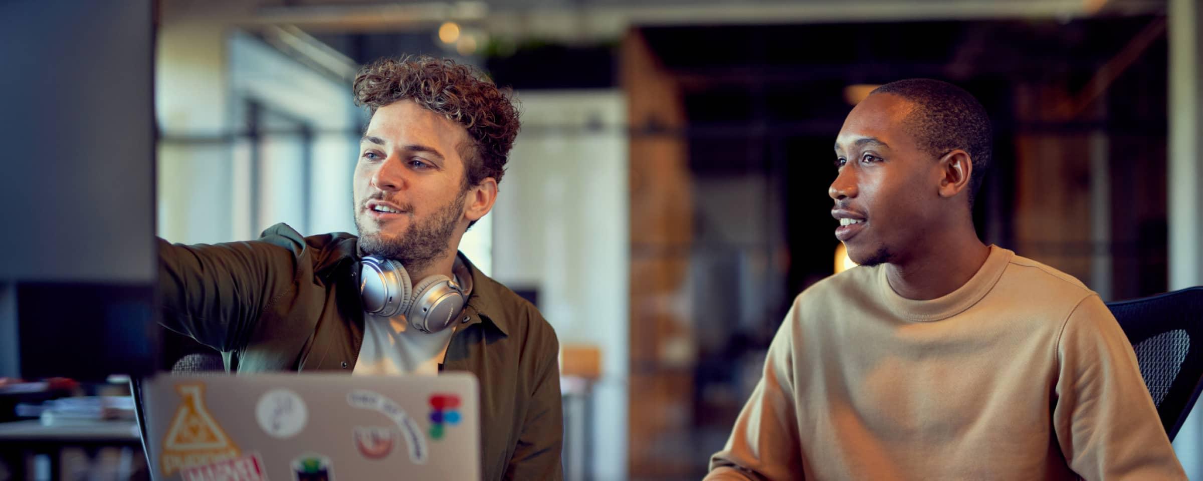 Twee personen die samenwerken aan een bureau met een laptop met verschillende stickers erop.
