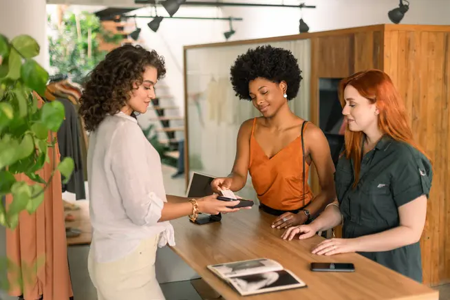Mulher com máquina de pagamento Adyen e duas clientes pagando com cartão