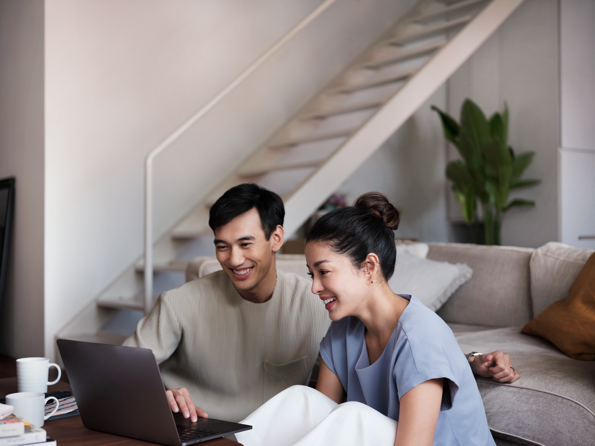 A smiling couple sitting in a cozy living room, completing payment on their laptop.