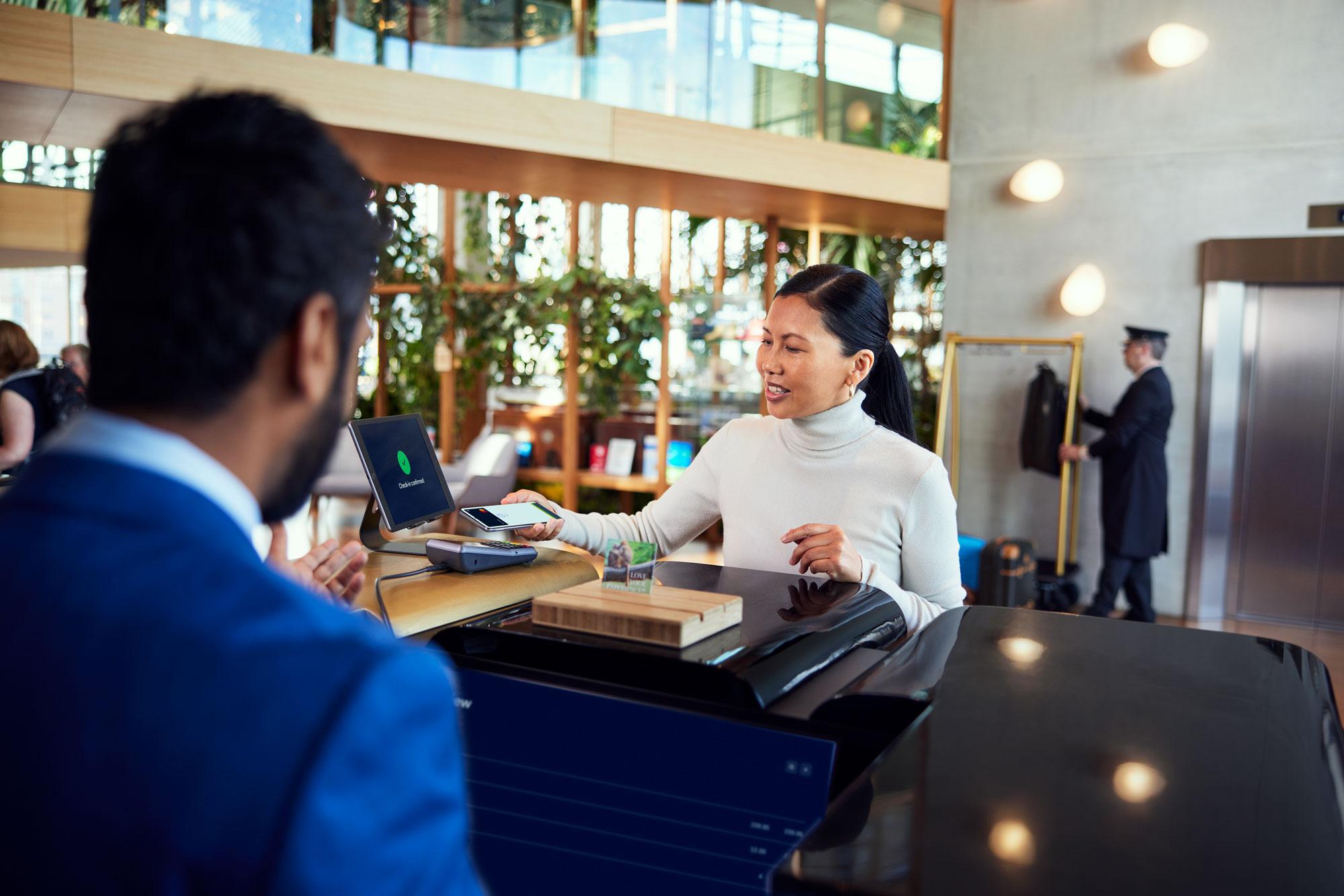 A woman at a hotel reception desk paying by tapping her smartphone at Adyen's terminal.