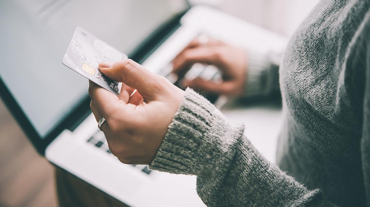 Primer plano de una persona que sostiene una tarjeta de crédito mientras utiliza una computadora portátil.