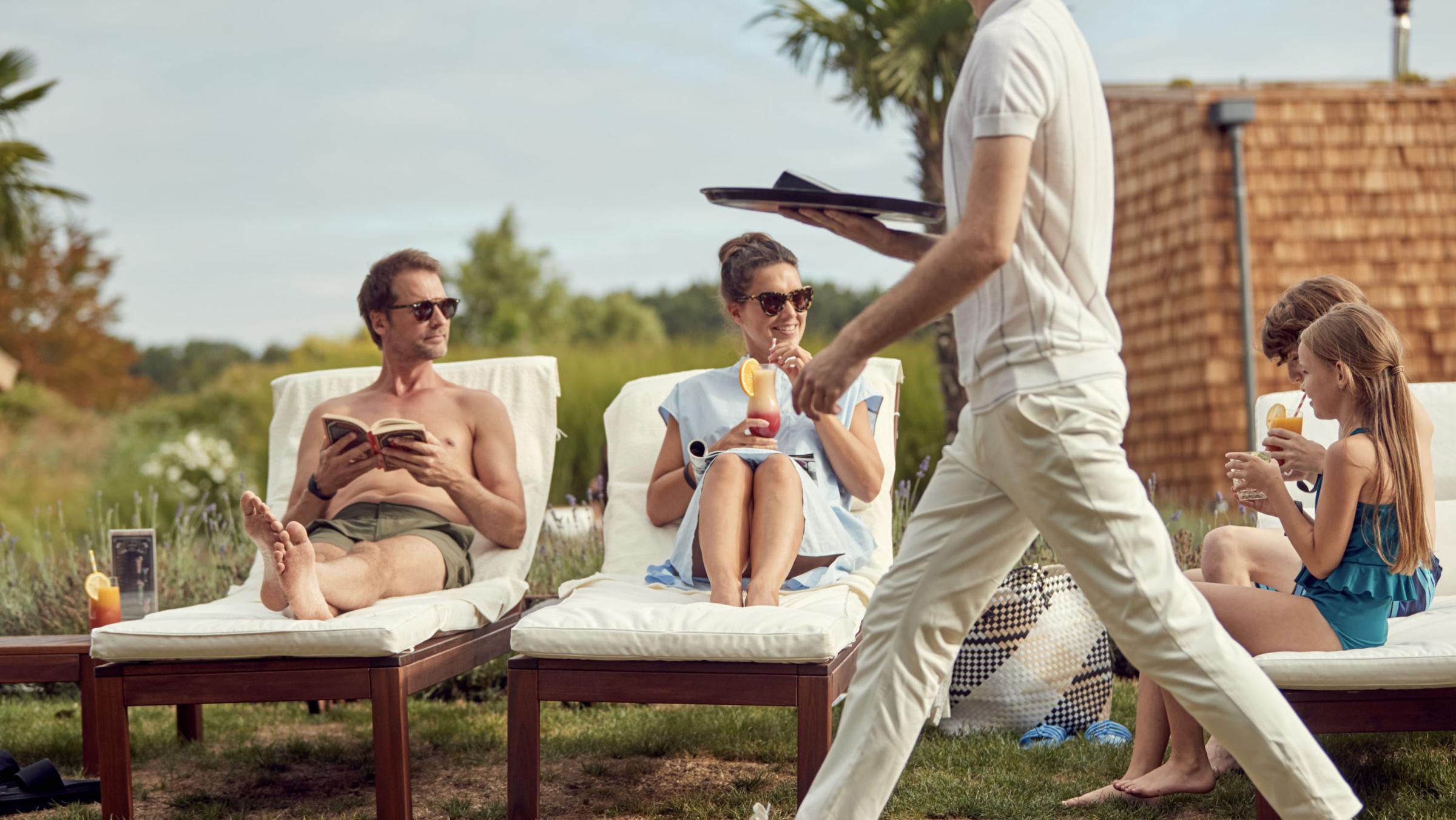 Group of people enjoying a sunny day outdoors with a waiter serving drinks.