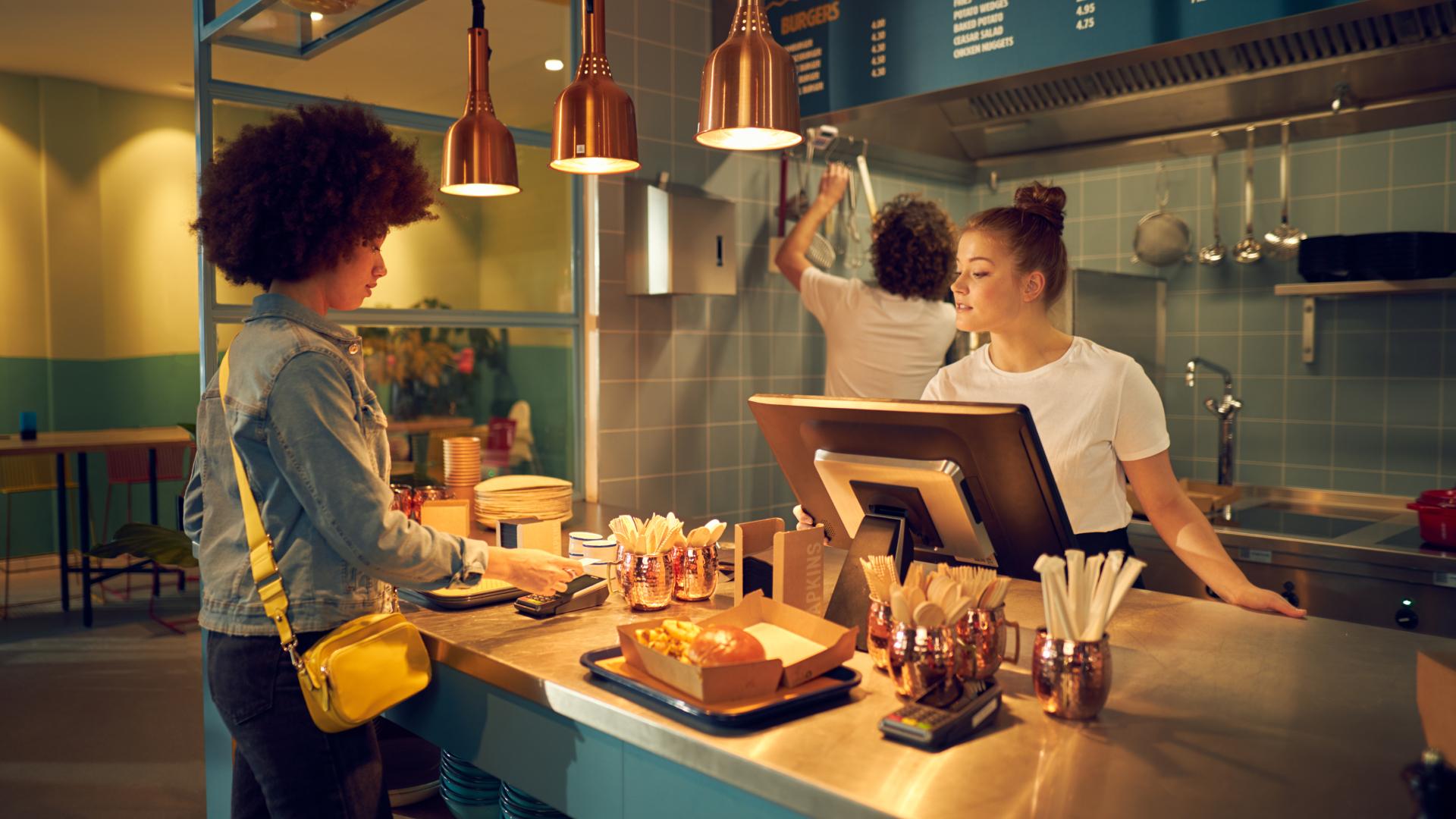 Kunde som betaler ved en restaurantdisk med en ansatt som hjelper