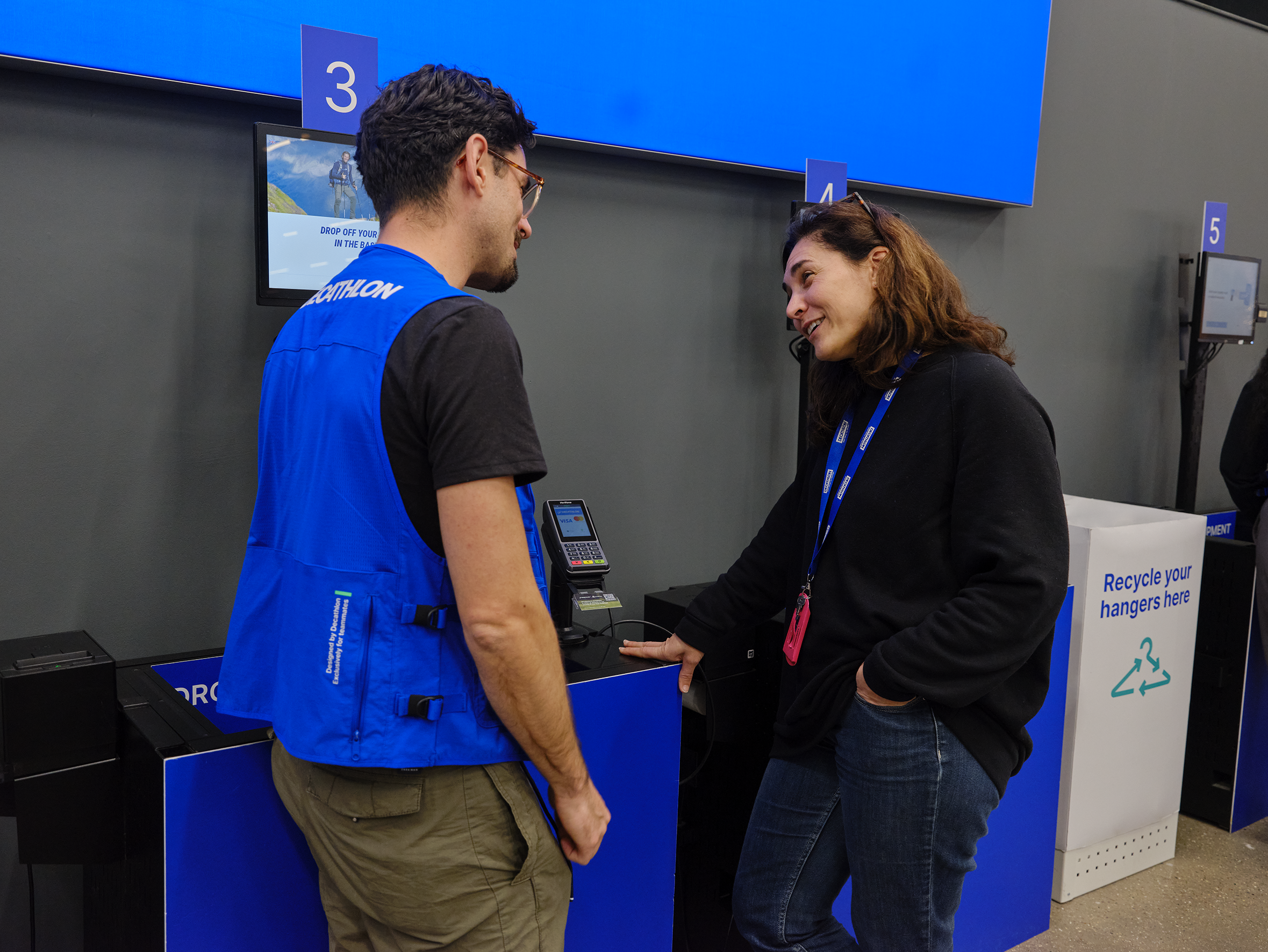 Decathlon employees chatting over Adyen's P400 Plus terminal at a checkout.