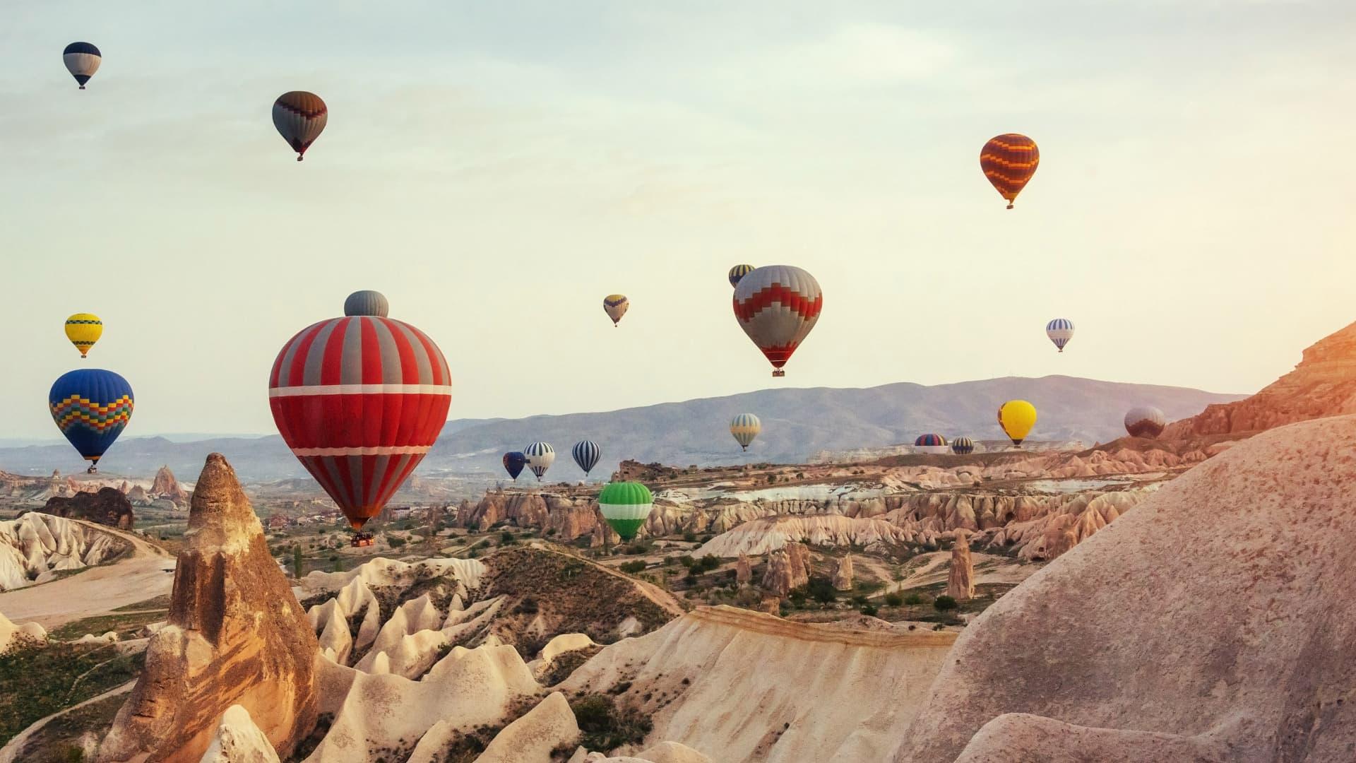 Kleurrijke luchtballonnen vliegen over unieke rotsformaties bij zonsopgang in Turkije.