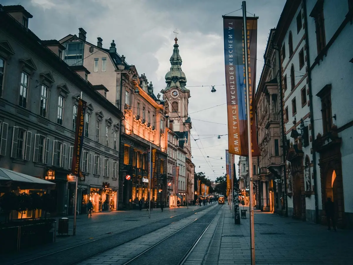 A street in Vienna with traditional European buildings at dusk, lit up with cozy lighting.