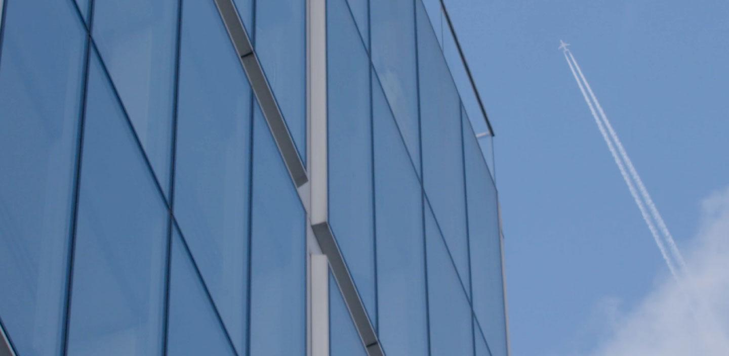 Façade de verre bleu d'un bâtiment moderne avec le ciel et un avion volant avec des traînées.