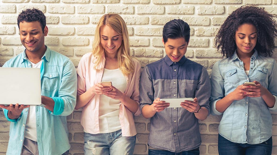 Quatro pessoas em pé contra uma parede de tijolo enquanto usam vários dispositivos digitais.