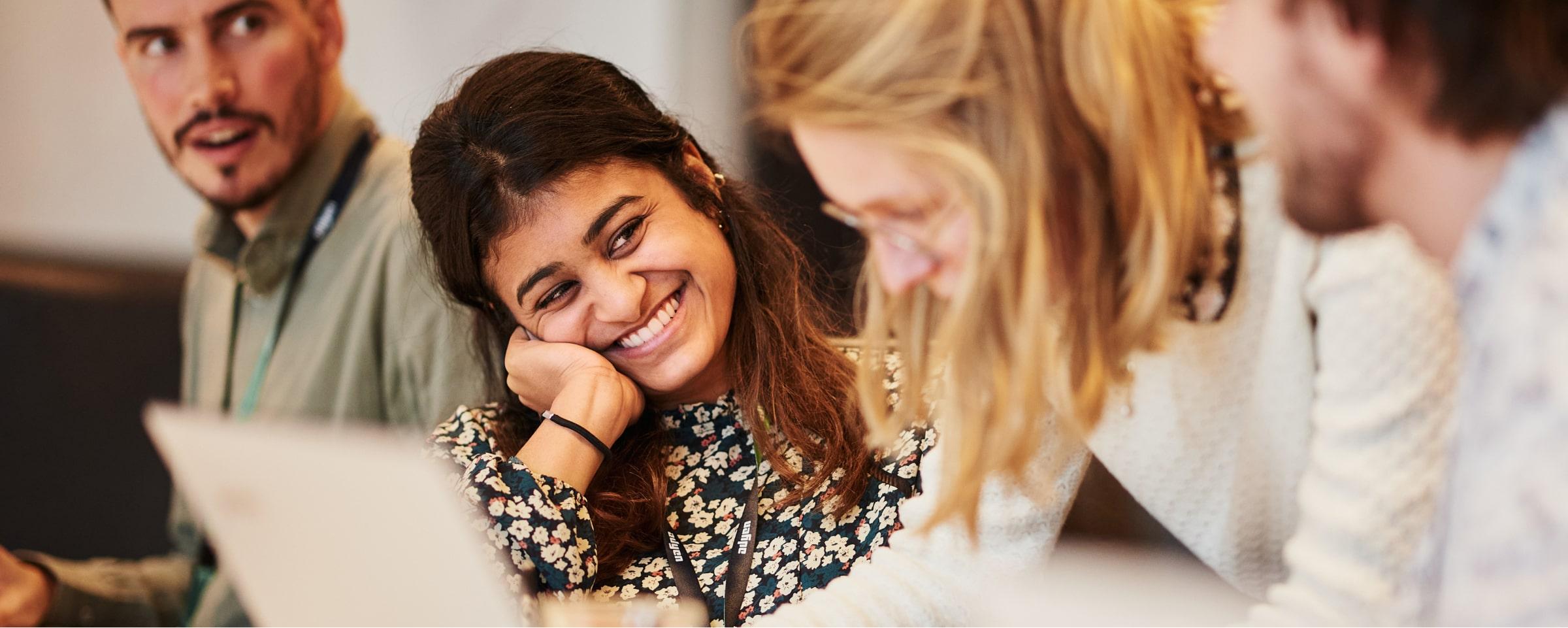 Three colleagues interacting in a casual office setting with one smiling woman in the foreground.