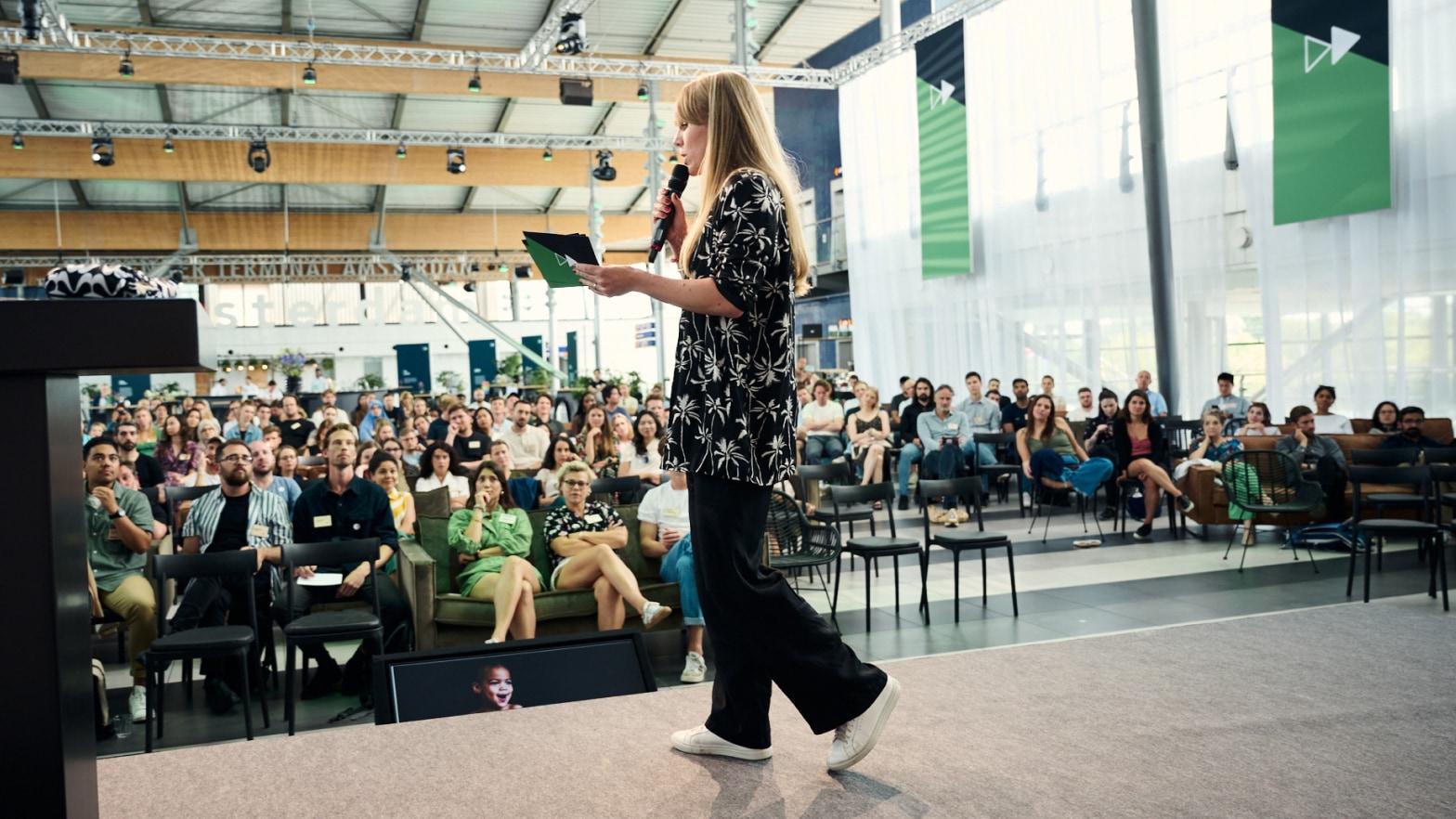 Speaker presenting to an audience at a conference with Adyen banners in the background.