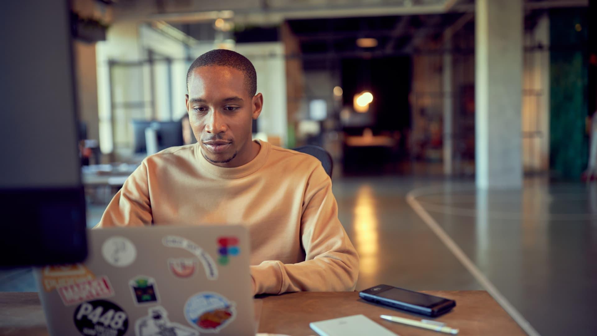Focused person working on laptop with stickers in a modern office space