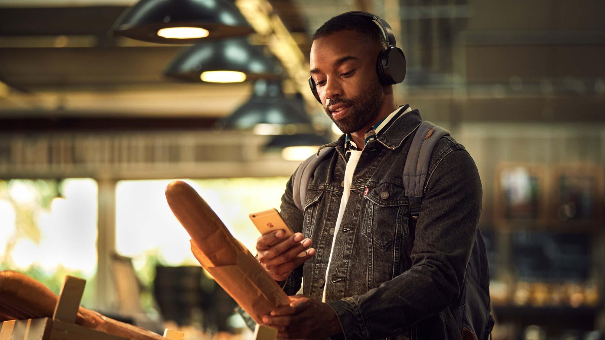 Mann mit Kopfhörern nutzt Smartphone in einer Bäckerei