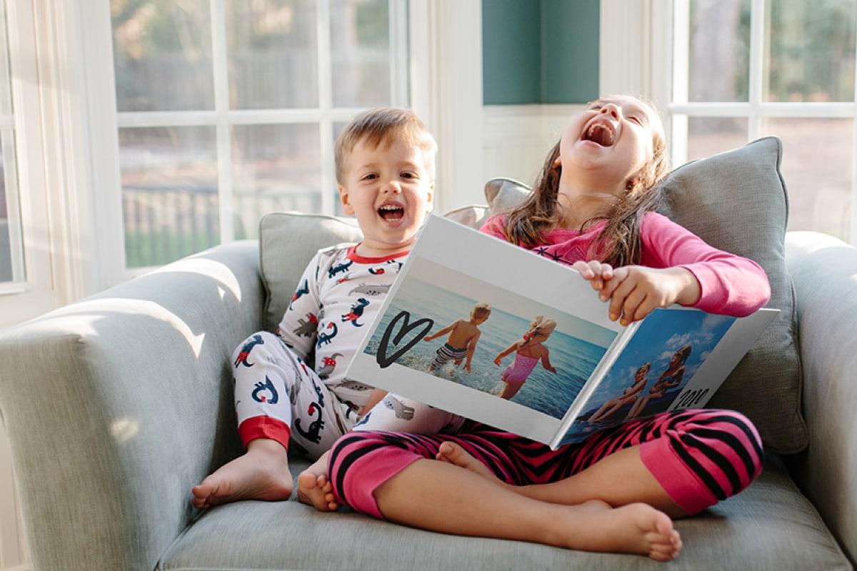 Twee kinderen die lachen en samen naar een fotoalbum kijken op een bank.